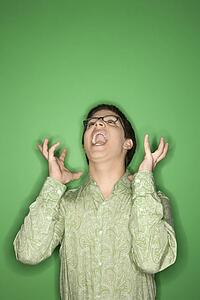Portrait of Caucasian teen boy screaming with hands beside ears in front of green background.