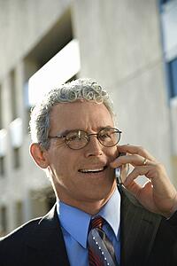 Prime adult Caucasian man in suit smiling and talking on cellphone in urban setting.