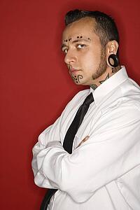 Caucasian mid-adult man with tattoos and piercings wearing necktie looking at viewer.