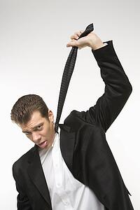 Caucasian mid-adult man pulling necktie out to choke himself while making facial expression.