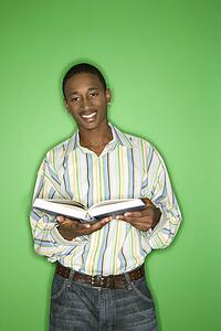 Portrait of smiling African-American teen boy holding a book standing in front of green background.