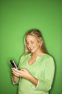 Portrait of blond Caucasian teen girl smiling at cellphone against green background.
