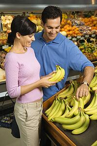 Caucasian mid-adult couple grocery shopping for bananas.