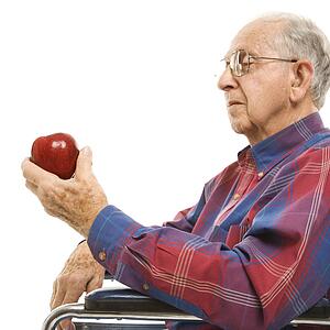 Profile of Caucasion elderly man sitting in wheelchair looking at red apple in his hand.