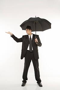 Caucasian mid-adult businessman wearing fedora holding umbrella with arm outstretched.
