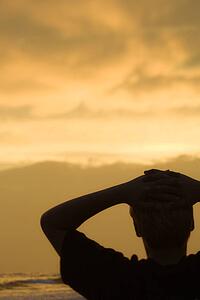 Caucasian pre-teen boy sihouette with hands behind head on beach at sunset.