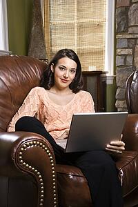 Caucasian/Hispanic young woman sitting in leather chair with laptop looking at viewer.