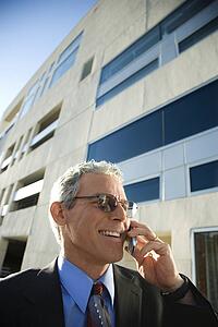 Prime adult Caucasian man in suit smiling and talking on cellphone in urban setting.