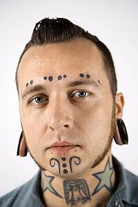 Caucasian mid-adult man with tattoos and piercings.