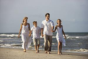 Caucasian family of four walking on beach.