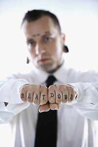 Caucasian mid-adult man with tattoos and piercings holding out fists reading beat down.