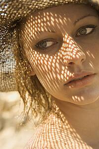 Close-up of young adult female Caucasian with shadow pattern from hat on face.