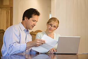 Caucasian mid-adult couple paying bills on laptop computer.
