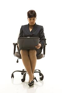 Filipino middle-aged businesswoman sitting in office chair with laptop against white background.