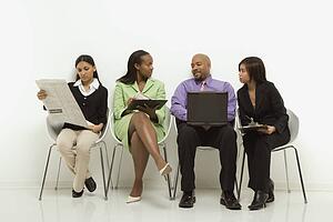 Multi-ethnic business group of men and women sitting looking at laptop and papers.