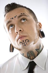 Caucasian mid-adult man with tattoos and piercings.