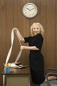 Mid-adult Caucasian female in vintage outfit holding a printout from calculator in her office.