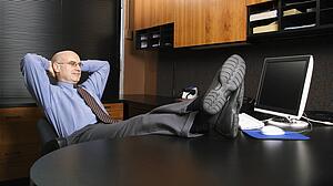 Caucasian middle-aged businessman in office sitting with feet on desk.