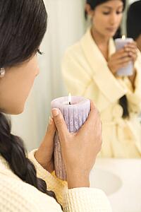 Asian/Indian young woman holding lit candle in front of mirror.