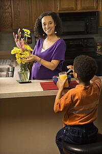 Portrait of young pregnant mother arranging flowers while son eats breakfast. 