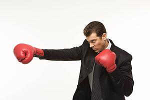 Caucasian mid-adult man wearing suit and punching with boxing gloves.