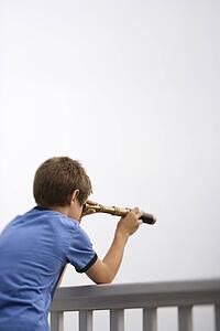 Caucasian pre-teen boy leaning on railing looking through telescope.