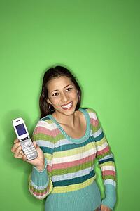 Portrait of smiling Multi-racial teen girl holding cellphone out standing in front of green background.