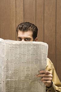 Caucasion mid-adult retro businessman peeking over top of newspaper.
