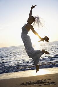 Young adult female Caucasian bride jumping on beach.