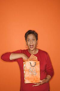 African American mature adult female with hand in gift bag looking surprised.