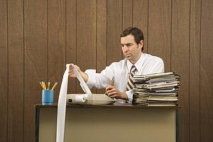 Mid-adult Caucasian male holding printout from calculator in office setting.
