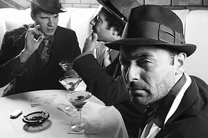 Three Caucasian prime adult males in retro suits sitting at table.