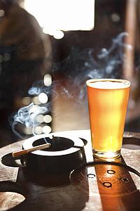 Full beer glass and cigarette with smoke rising in nightclub.