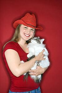 Young Caucasian female adult holding cat wearing cowboy hat.