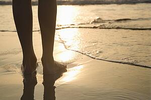 Caucasian person standing barefoot on beach in water.