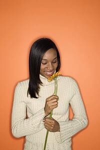 Portrait of smiling African-American teen girl holding single Gerbera Daisy standing against orange background.