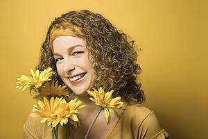 Portrait of smiling young adult Caucasian woman on yellow background holding bouquet of flowers.