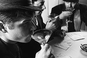 Three Caucasian prime adult males in retro suits sitting at table drinking cocktails.
