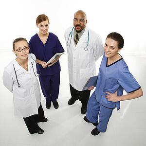 Full-length portrait of African-American man and Caucasian women medical healthcare workers smiling in uniforms standing against white background.
