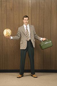 Mid-adult Caucasian male in retro suit holding luggage and a globe.