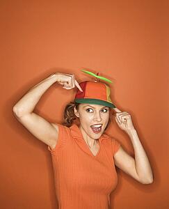 Smiling Caucasian mid-adult woman pointing and wearing propeller cap on orange background.