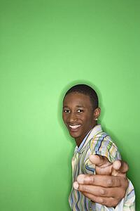 Portrait of smiling African-American teen boy holding hand out toward viewer against green background.