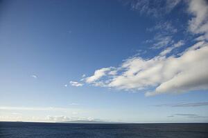 Blue sky with fluffy white clouds over ocean horizen.