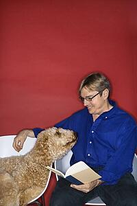 Middle-aged Caucasian man with Goldendoodle dog reading book.
