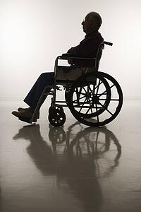 Profile view of silhouetted Caucasion elderly man sitting in wheelchair.