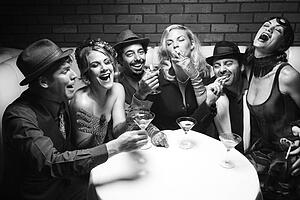 Group of Caucasian prime adult retro males and females sitting at table in lounge laughing.