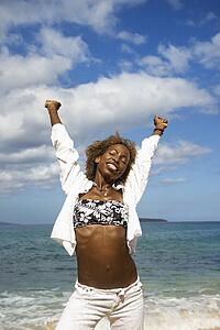 Mid-adult African-American female stretching arms with ocean in background.