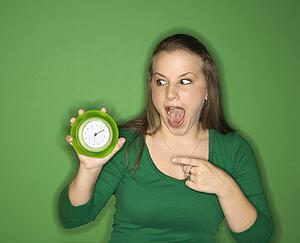 Young female Caucasian adult holding and pointing to clock.