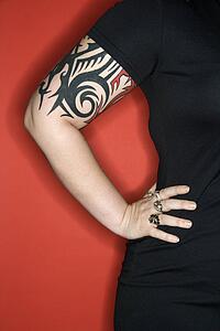 Caucasian woman's tattooed arm with hand on hip against red background.