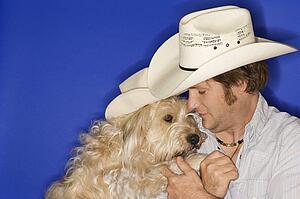 Fluffy brown dog and male Caucasian young adult wearing cowboy hats.